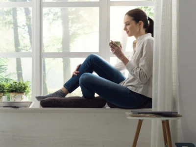 A woman sits near a window enjoying a warm beverage.