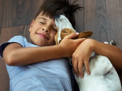A little boy sits on the floor and plays with his dog.