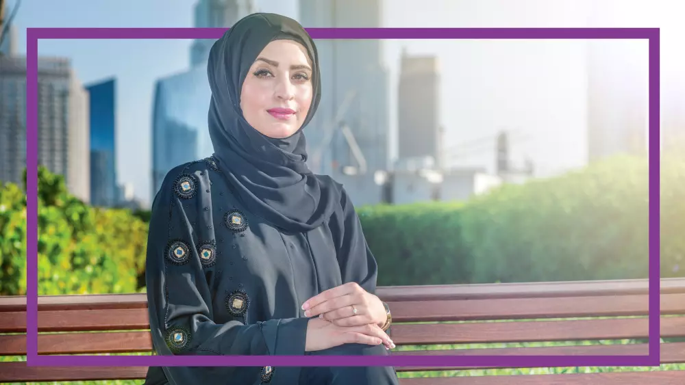 A woman confidently sitting outdoor in front of some trees.