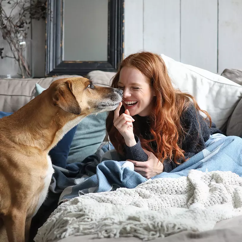 A woman plays with her dog, while sitting on her sofa.