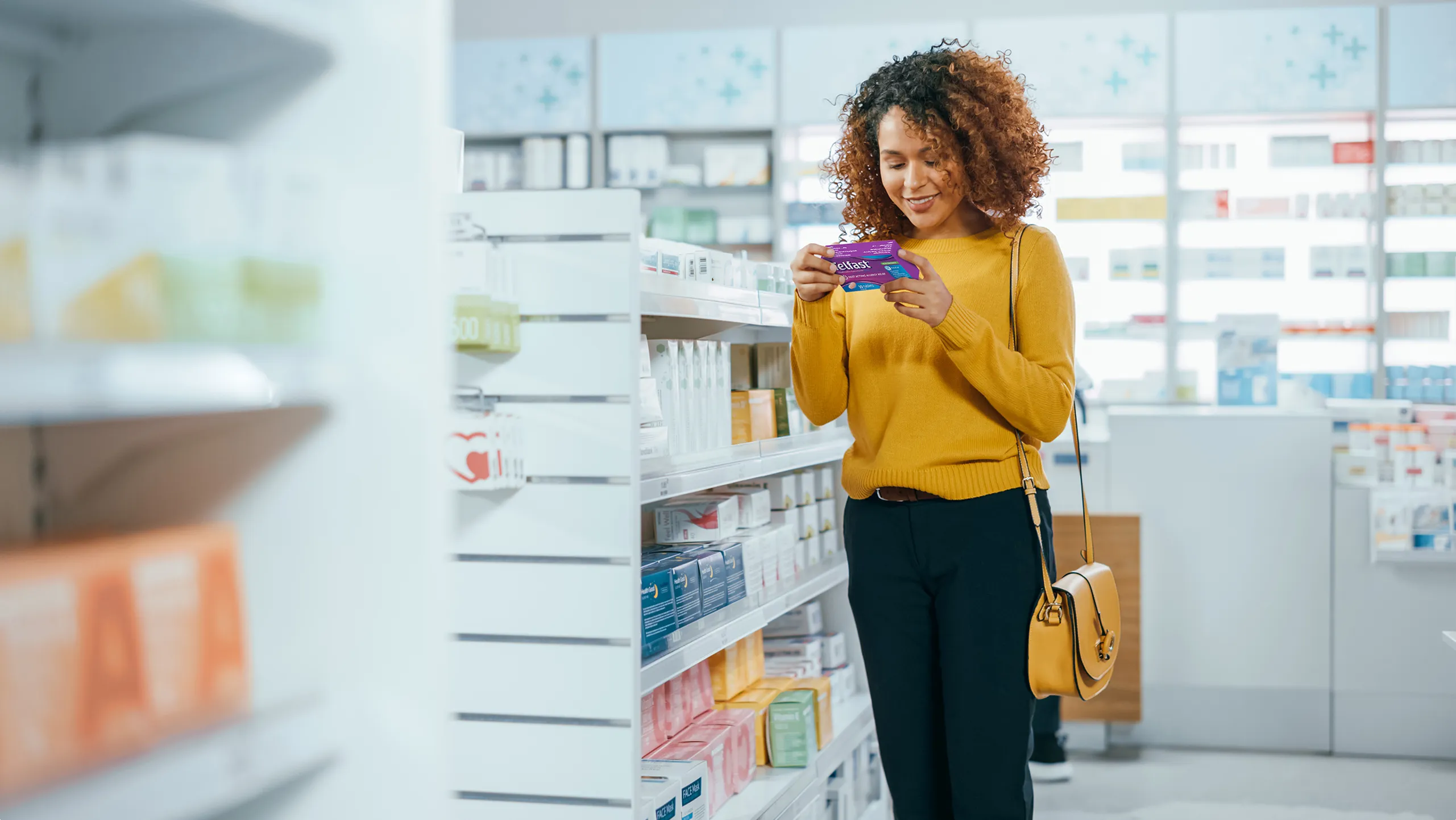 A Woman comparing Telfast® with another medicine in the allergy aisle at a store, looking approvingly towards Telfast®.