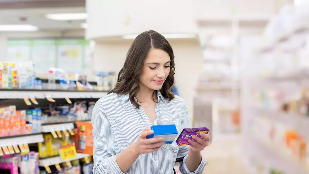 A Woman comparing Telfast® with another medicine in the allergy aisle at a store, looking approvingly towards Telfast®.